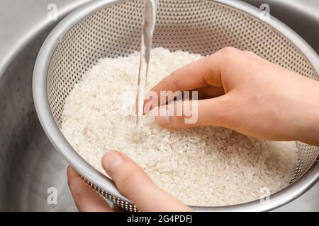 Woman rinsing rice in sifter under running water, closeup Stock Photo
