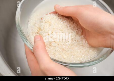 Woman rinsing rice in glass bowl under running water, closeup Stock Photo