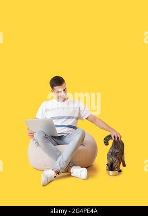 Young man with cute cat using laptop on color background Stock Photo