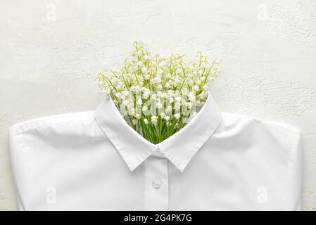 Creative composition with white shirt and lily-of-the-valley flowers on light background Stock Photo