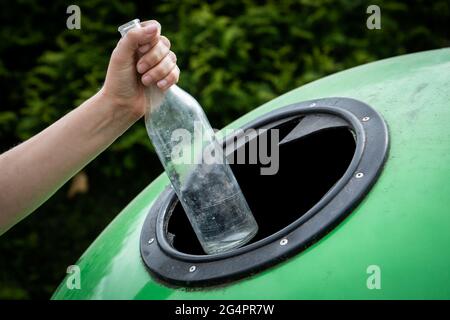 Throwing empty glass bottle into green recycle bin garbage container. Waste Sorting And Recycling Concept. Stock Photo