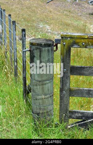 Paddock wire fence with thick pole holding heavy timber gate on bolted hinges. Stock Photo