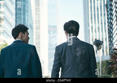 rear view of two asian corporate businessmen walking talking in central business district in modern city Stock Photo