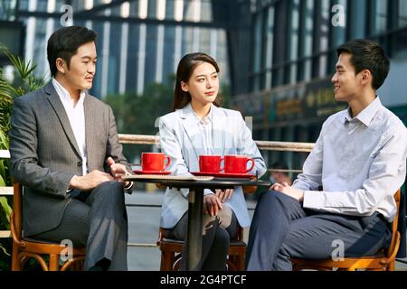 three asian corporate businesspeople discussing business outdoors in coffee shop Stock Photo