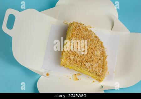 The cake is packaged in a white paper box on a light blue background. Open Kraft packaging with a piece of sweet layer cake. Eco-friendly Lunch Box. F Stock Photo