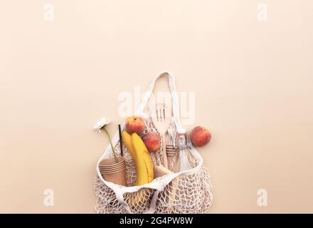 Eco friendly summer conceptual flat lay on beige background with eco shopping bag, kitchen recycling cutlery, glass bottle of water, bananas and apple Stock Photo