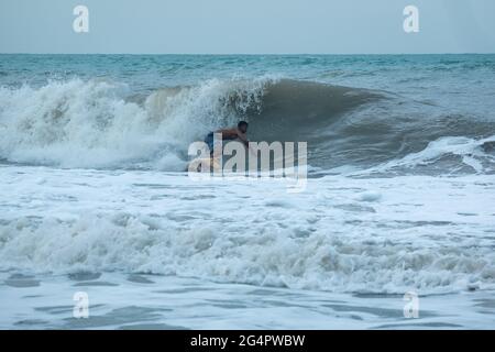 Palomino, Dibulla, La Guajira, Colombia - May 24 2021: Young Latin Surfing in the Ocean Waves at Sunset under a Cloudy Sky Stock Photo