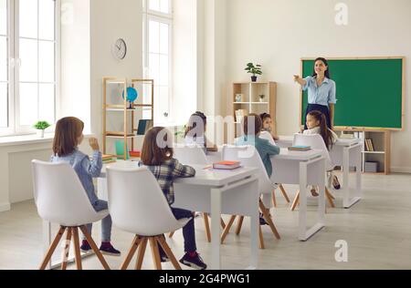 Little elementary school student raises hand and answers teacher's question in class Stock Photo