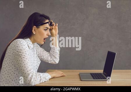 Side view of a young woman with a shocked expression looking at a laptop screen. Stock Photo