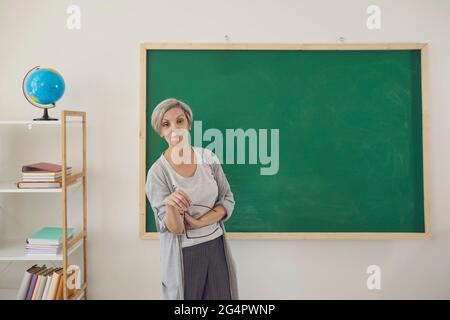 School education. Senior teacher explaining material near blackboard at clasroom. Stock Photo