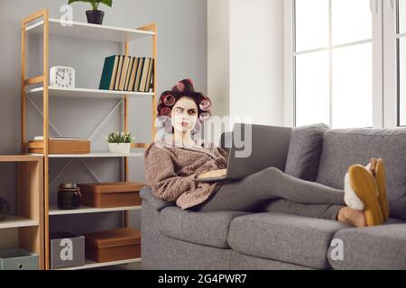 Funny angry woman sitting on sofa with laptop and reading nasty comments on social media Stock Photo