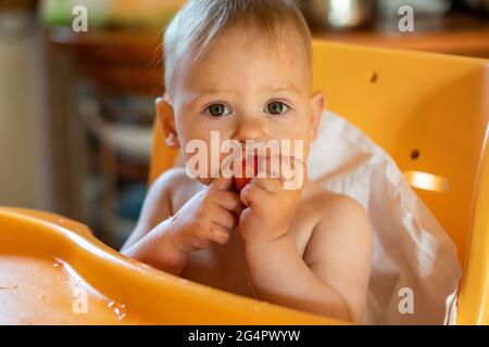 Baby or toddler with dirty face eating strawberry in home kitchen Stock Photo