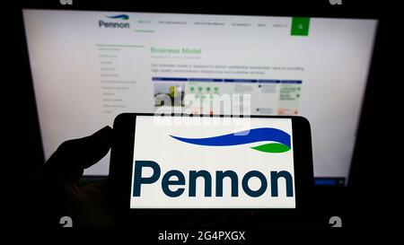 Person holding cellphone with logo of British water utility company Pennon Group plc on screen in front of business webpage. Focus on phone display. Stock Photo