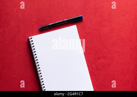 A notebook of white paper with a marker placed on a red background Stock Photo