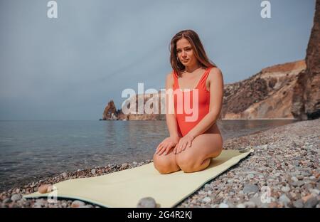 Young woman in red swimsuit with long hair practicing stretching Stock Photo
