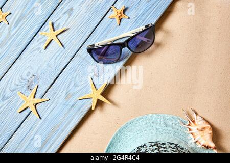 Summer background from sea sand with seashell, hat, sunglasses and starfish on blue wooden planks. Top view with copy space Stock Photo