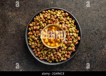 Canned pet food and dried kibble on plate. Tasty food for dog or cat on black table. Top view. Stock Photo