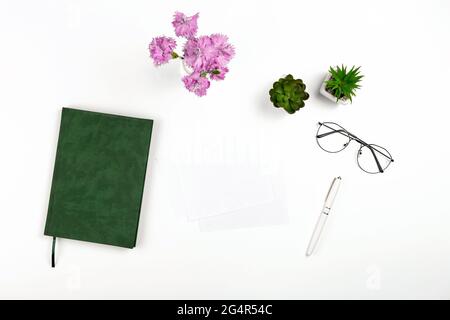 Light postcard mockup for design presentation on a white workplace with notebook, pen, glasses and flowers. Stock Photo