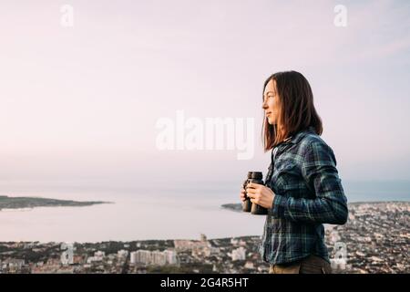 Young woman traveler holding binoculars in hands. Stock Photo