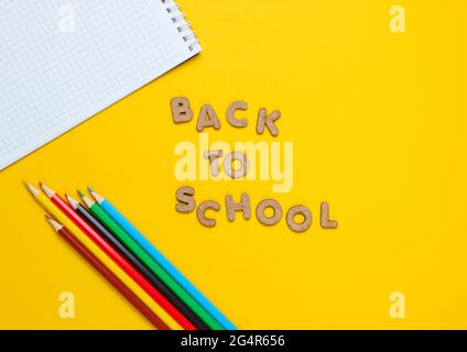 School time concept. Multicolored pencils, notebook on yellow background and words back to school with wooden letters Stock Photo