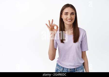 Zero problems, alright. Young smiling woman shows okay OK sign and nod in approval, like and agree gesture, approve something good, excellent job Stock Photo