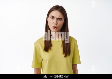You say what. Confused and annoyed woman making creepy strange face, grimacing and raising eyebrow suspicious, staring at camera puzzled, standing Stock Photo