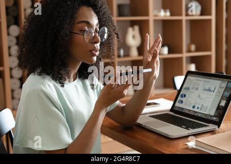 Young african american woman dictating voice message to client, chatting with friend, recording audio Stock Photo