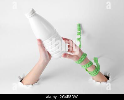 The concept of losing weight. Female hands hold a bottle of kefir with a ruler through the torn holes of white background Stock Photo