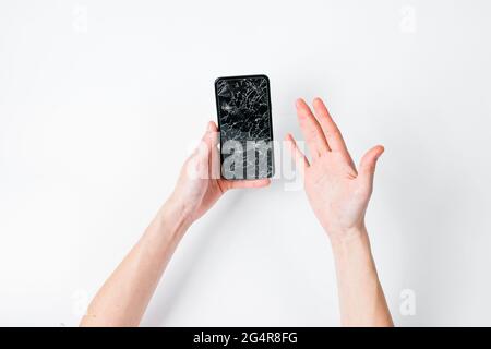 Female hands hold a smartphone with a broken screen through torn hole of white background Stock Photo