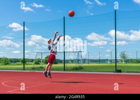 Attractive young boy shooting ball to the hoop at playground.cute young boy plays basketball on the playground in the summer warm day. Stock Photo