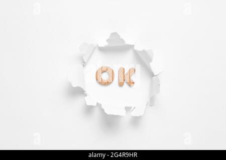 Word ok in torn hole on white background. Stock Photo