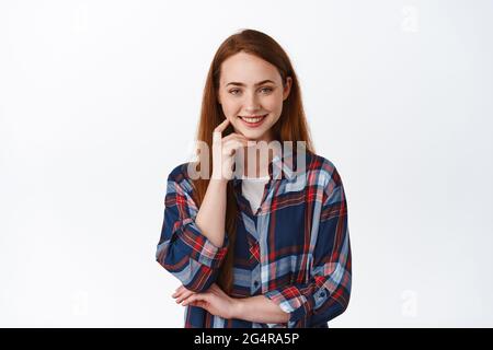 Smiling candid redhead girl, natural look with relaxed emotion, smile white teeth, look determined and ready, made her decision, standing over white Stock Photo