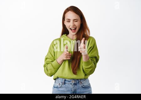 Nice work, congrats. Smiling redhead woman winking and pointing finger pistols at camera, choosing you, say congratulations, praise good job, white Stock Photo