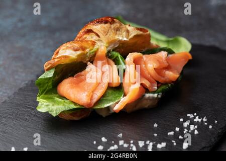 Fresh baked croissant sandwich with salad and salmon on a black slate board Stock Photo