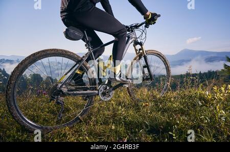 Close up, low angle view on a bike with cyclist. Man's legs riding his bicycle on grass in summer in the mountains against blue sky. Concept of extreme cycling Stock Photo