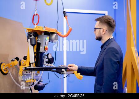 Worker engineer uses vacuum conveyor to move flat load in factory, production optimization concept. Stock Photo