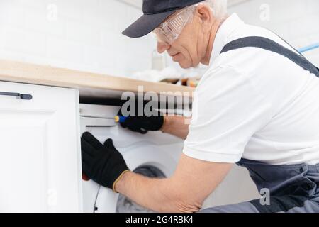 Service for repair, plumber man in uniform repairing washing machine. Stock Photo