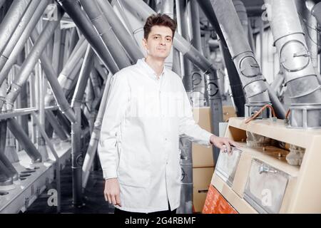 Operator checks quality of finished food products wheat flour. Modern electrical mill machinery for production. Stock Photo