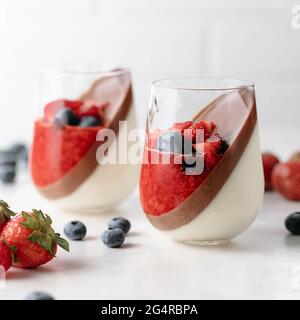 Double-layer vanilla and chocolate panna cotta dessert with with strawberry puree, fresh blueberries and strawberries on white background Stock Photo