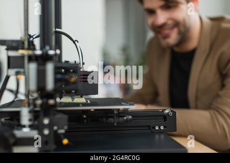 3D printer producing plastic model near blurred young smiling man in modern office Stock Photo