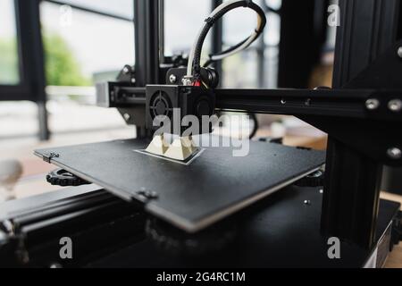 3D printer creating plastic model on table in modern office Stock Photo