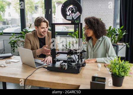 young interracial colleagues working with 3D printer and laptop in modern office Stock Photo