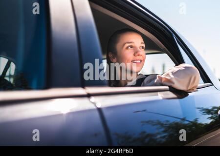 Passenger in taxi or woman in car sitting on the backseat looking outside the window. Happy female customer in cab. Elegant smiling businesswoman. Stock Photo