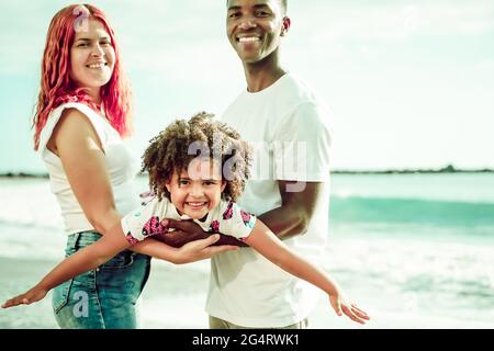 Happy multiethnic family, daughter simulating flying with her arms. Summer, holiday and family concept.