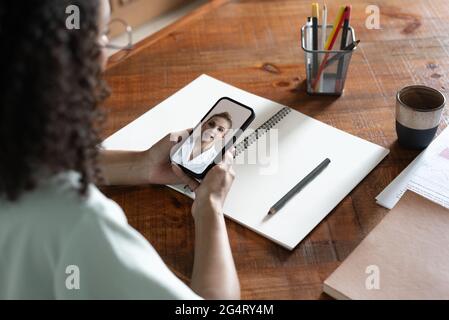 Young african american woman entrepreneur having a videocall with doctor, holding mobile phone in the office. Stock Photo
