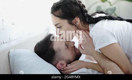 Young brunette woman kissing boyfriend in leather jacket near tree in ...