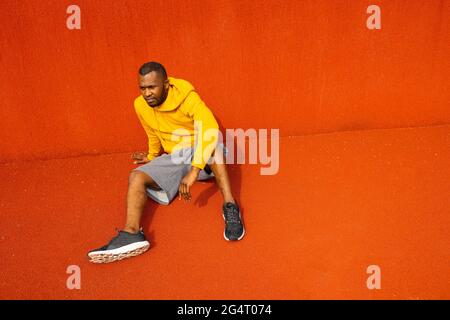African-American sportsman athlete having break rest after doing sport exercises workout alone. Fitness coach in trendy yellow sportswear showing Stock Photo