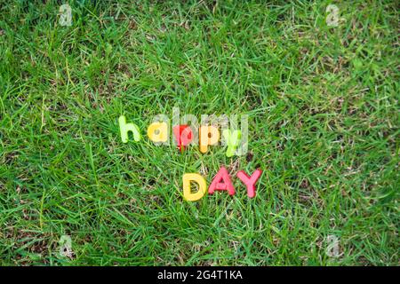 happy day lettering written with toy letters on the grass in the garden of the house Stock Photo