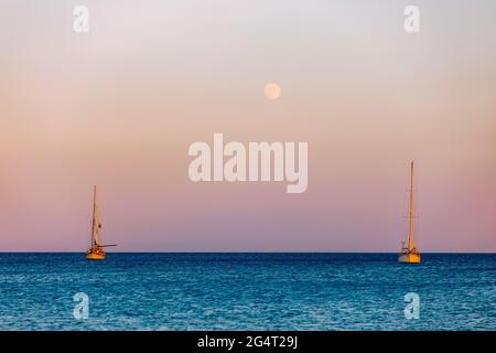 Full moon rising over the water with a small sailing boat in the foreground. Sailing boat with raising moon at sunset. Moon rising over the sea and ya Stock Photo