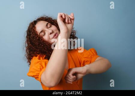 Joyful redhead curly girl smiling and dancing on camera isolated over blue background Stock Photo